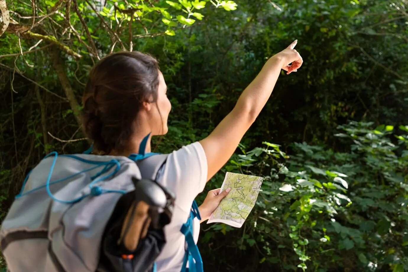 A woman with a backpack points while holding a map.